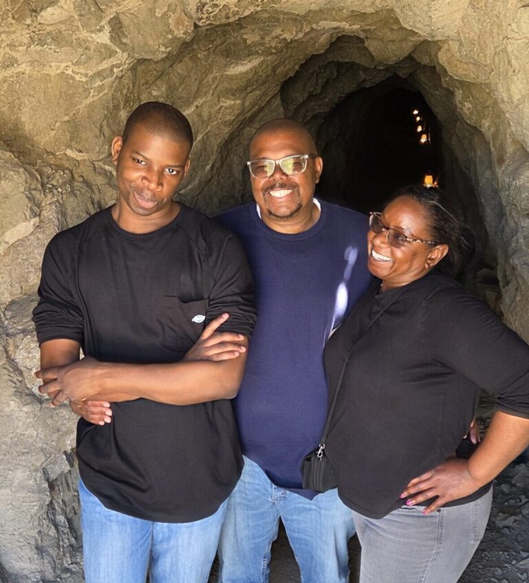Smiling group at Nevada’s rocky tunnel entrance near Colorado River, sunlight shining—perfect for ATV tours and Ghost Town sightseeing.