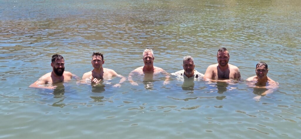 Six men smile in waist-deep Colorado River water near Las Vegas, Nevada, under clear skies—ideal for ATV tours or RZR adventures.
