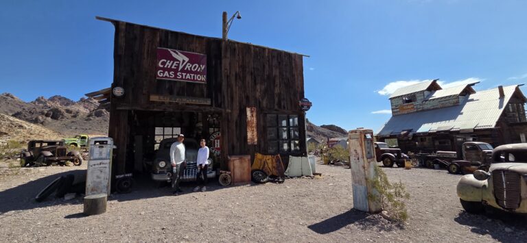 Two people at a vintage Chevron gas station near Las Vegas, Nevada—classic cars, desert views, perfect for ghost town tours.
