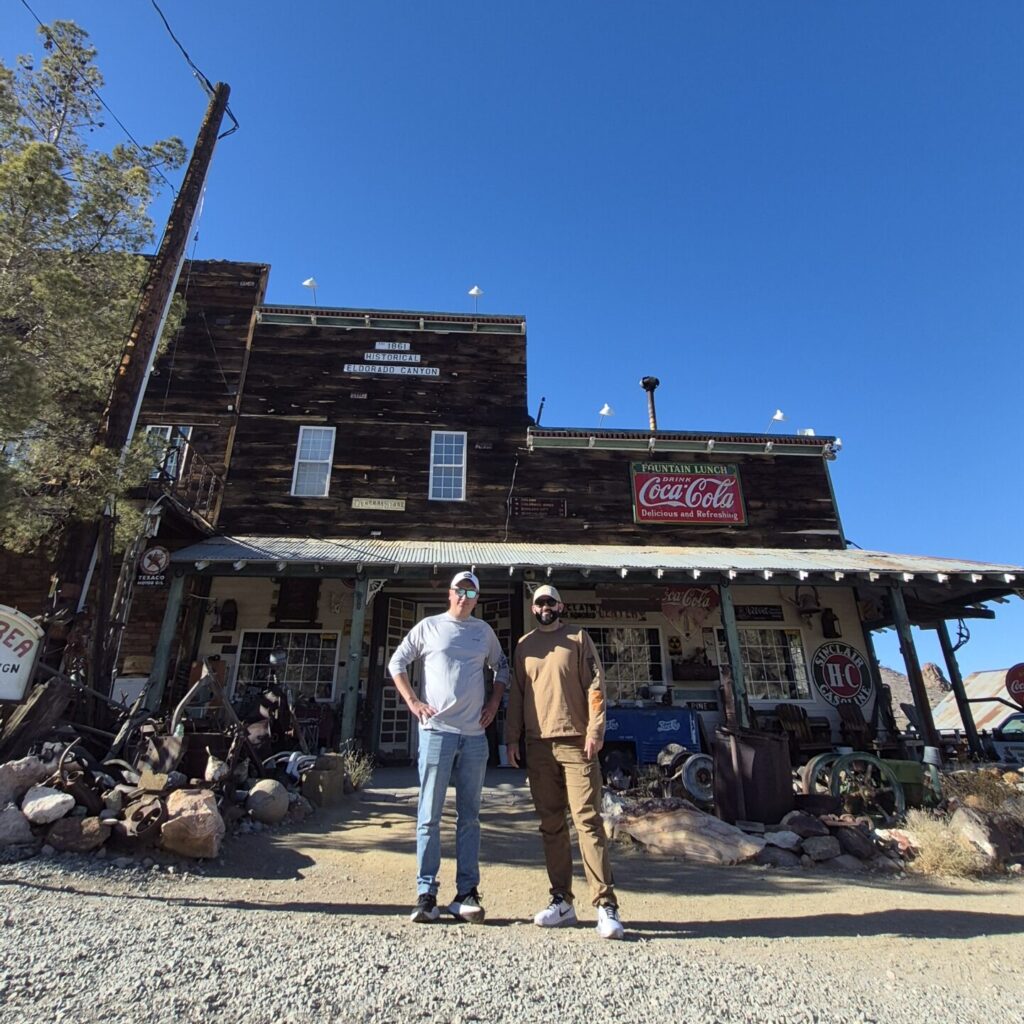 Two people at a Nevada ghost town’s wooden building with vintage Coca-Cola sign—perfect for Las Vegas ATV tours or sightseeing.