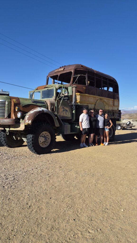 Group posing by a vintage rusted military truck near Las Vegas on a Nevada desert Ghost Town sightseeing adventure.
