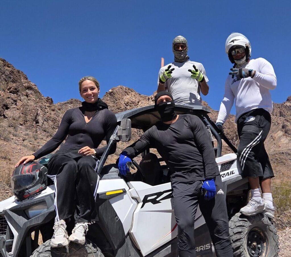 Adventurers in sporty gear pose by an ATV in Nevada desert near Las Vegas on a thrilling RZR off-road tour under blue skies.