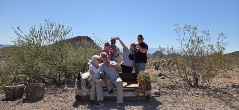 Six friends smile on a rusted car seat in Nevada desert near Las Vegas, perfect for ATV tours or Ghost Town sightseeing.