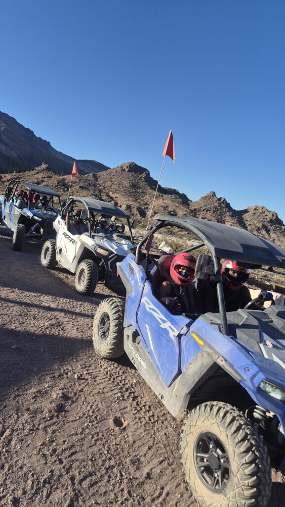 ATV tour near Las Vegas: three off-road vehicles with orange flags ride a rocky Nevada trail, mountains in the background.