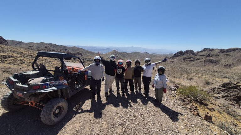 Six people in helmets on rocky Nevada terrain with an ATV, near Las Vegas mountains—perfect for RZR off-road tours.