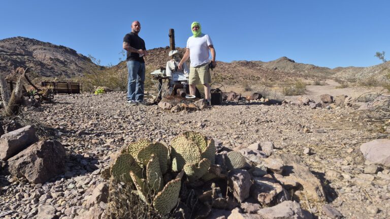 Two men near a table with gear in Nevada’s desert, cactus and mountains nearby, ready for Las Vegas ATV or RZR off-road tours.