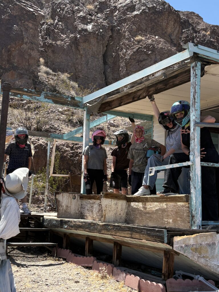 Group in helmets and casual wear stand on a Nevada ghost town porch, ready for ATV tours near the Colorado River by Las Vegas.