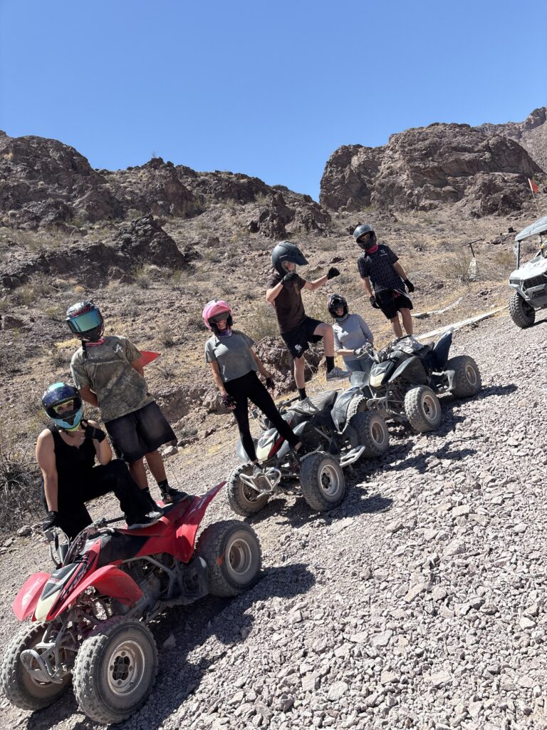 Group on ATVs, helmets on, posed in Nevada desert with rugged hills—Las Vegas ATV tour adventure under clear blue sky.
