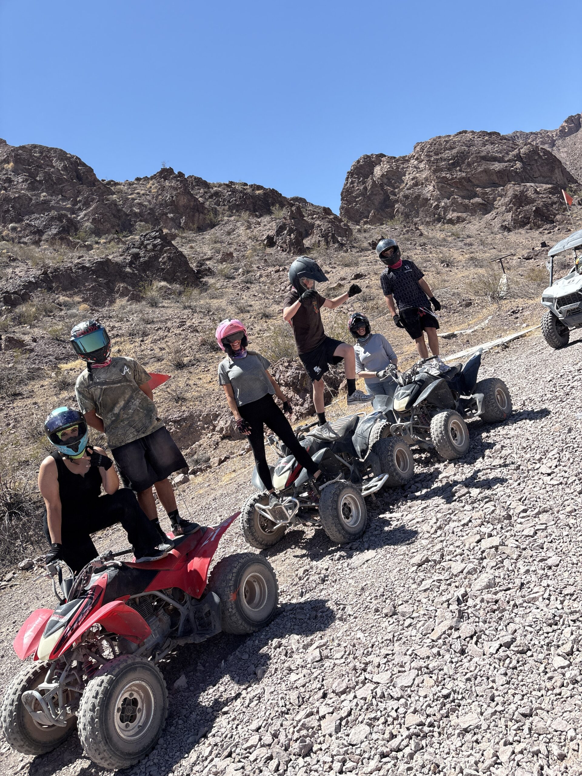 Group on ATVs, helmets on, posed in Nevada desert with rugged hills—Las Vegas ATV tour adventure under clear blue sky.