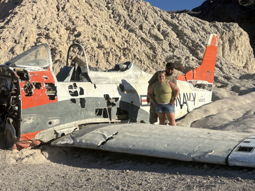 Two people by a weathered Navy plane wreck in a rocky desert near Las Vegas, perfect for Nevada ATV tours or Ghost Town sightseeing.