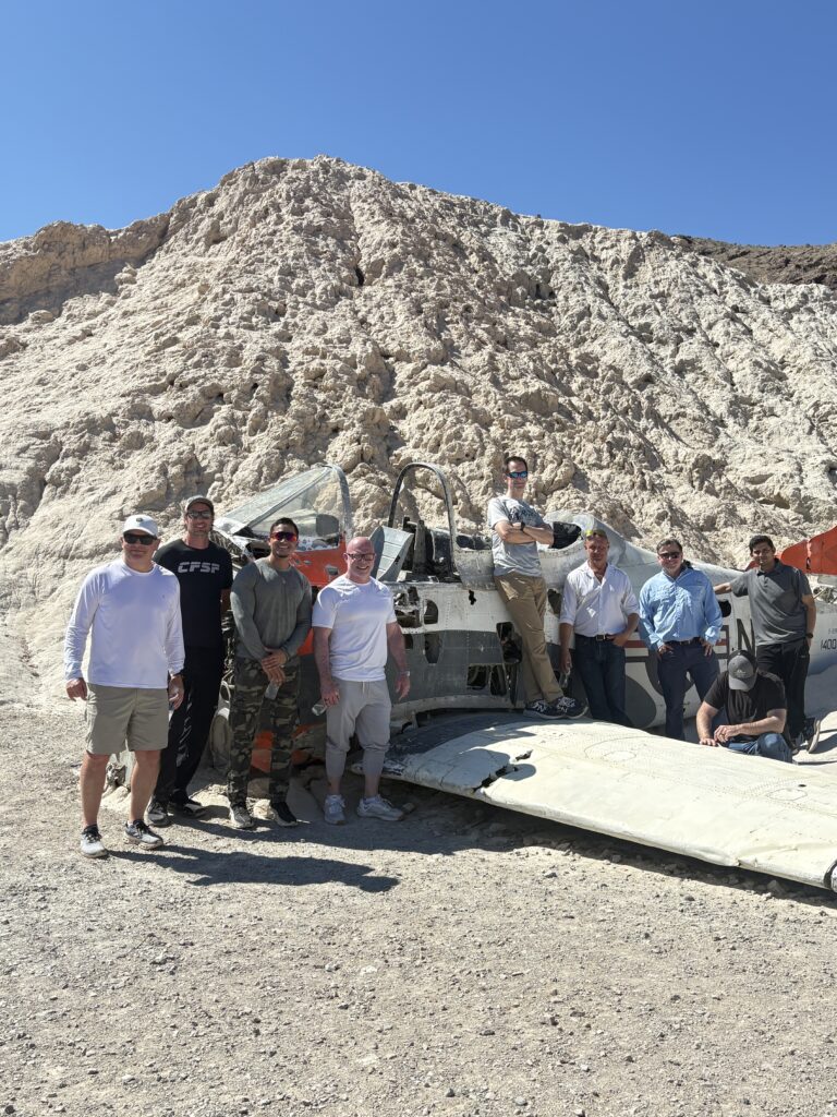 Eight men pose by a crashed plane in Nevada’s rocky desert near Las Vegas, perfect for ATV tours and Ghost Town sightseeing.