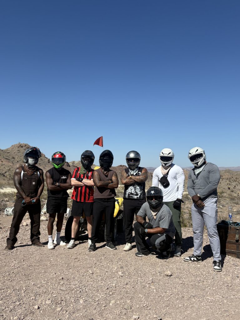 Group of seven in helmets on Nevada desert, ready for Las Vegas ATV tour near Colorado River with mountain backdrop.