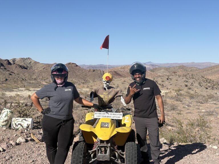 ATV riders in helmets pose on a Nevada desert trail near Las Vegas, enjoying an off-road adventure under a clear blue sky.