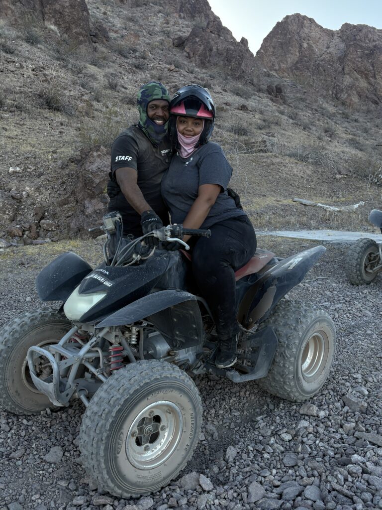 Smiling riders in helmets enjoy a Nevada ATV tour on rocky terrain near the Colorado River and Las Vegas desert hills.