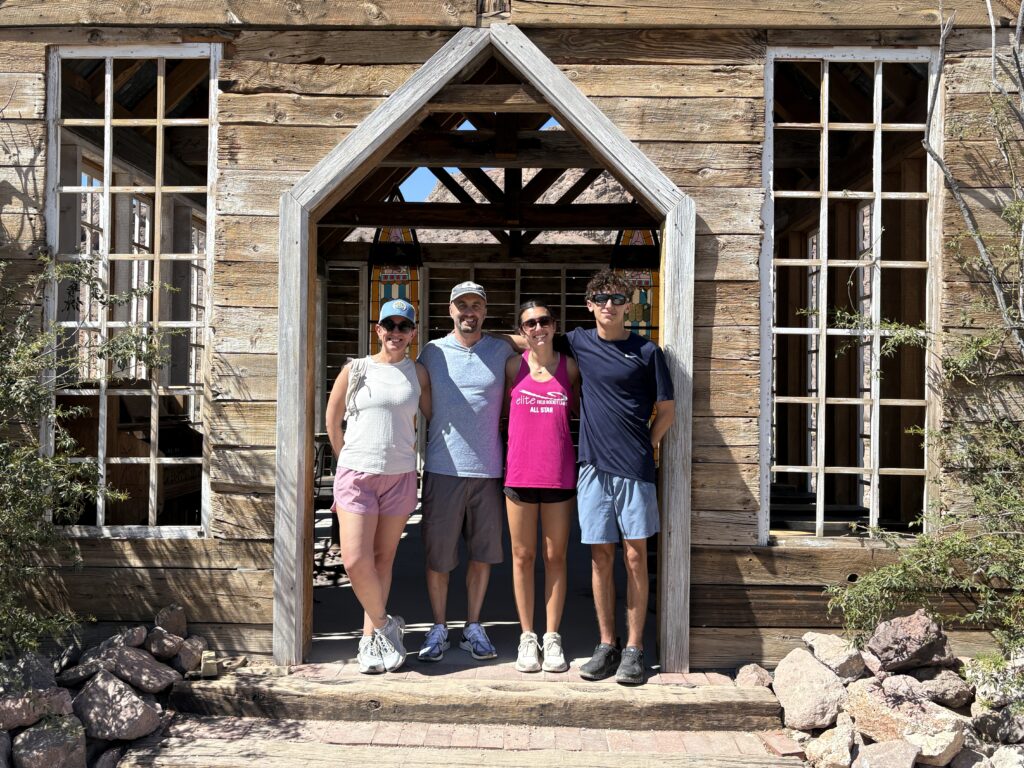 Group smiles at rustic wooden building entrance near Nevada’s Colorado River, ready for Ghost Town sightseeing on a sunny day.