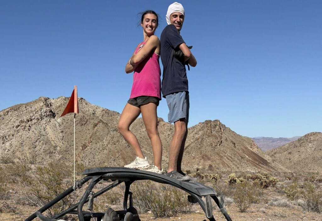 Two people stand atop a Polaris RZR in Nevada’s rocky desert, red flag flying—perfect for Las Vegas ATV tours and off-road adventures.