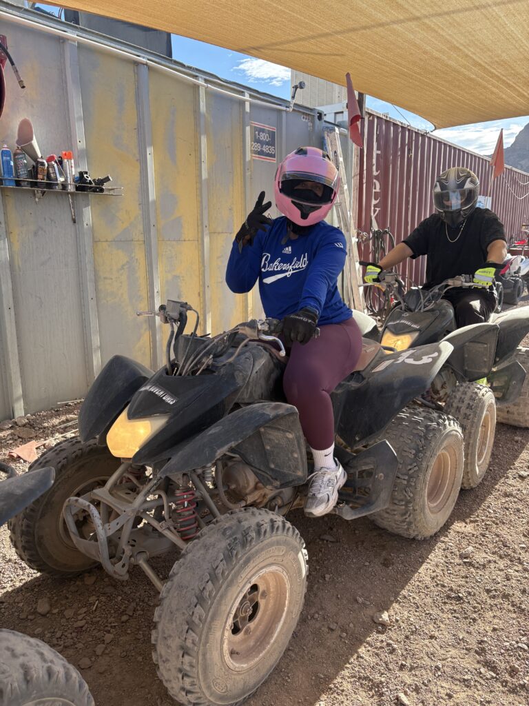 Riders on ATVs make a peace sign during a Las Vegas ATV tour near the Colorado River, under a canopy on the desert terrain.