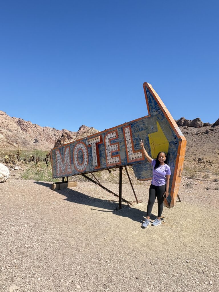 Visitor by a vintage arrow-shaped MOTEL sign in a Nevada desert near rocky hills, ideal for ATV tours or Ghost Town sightseeing.