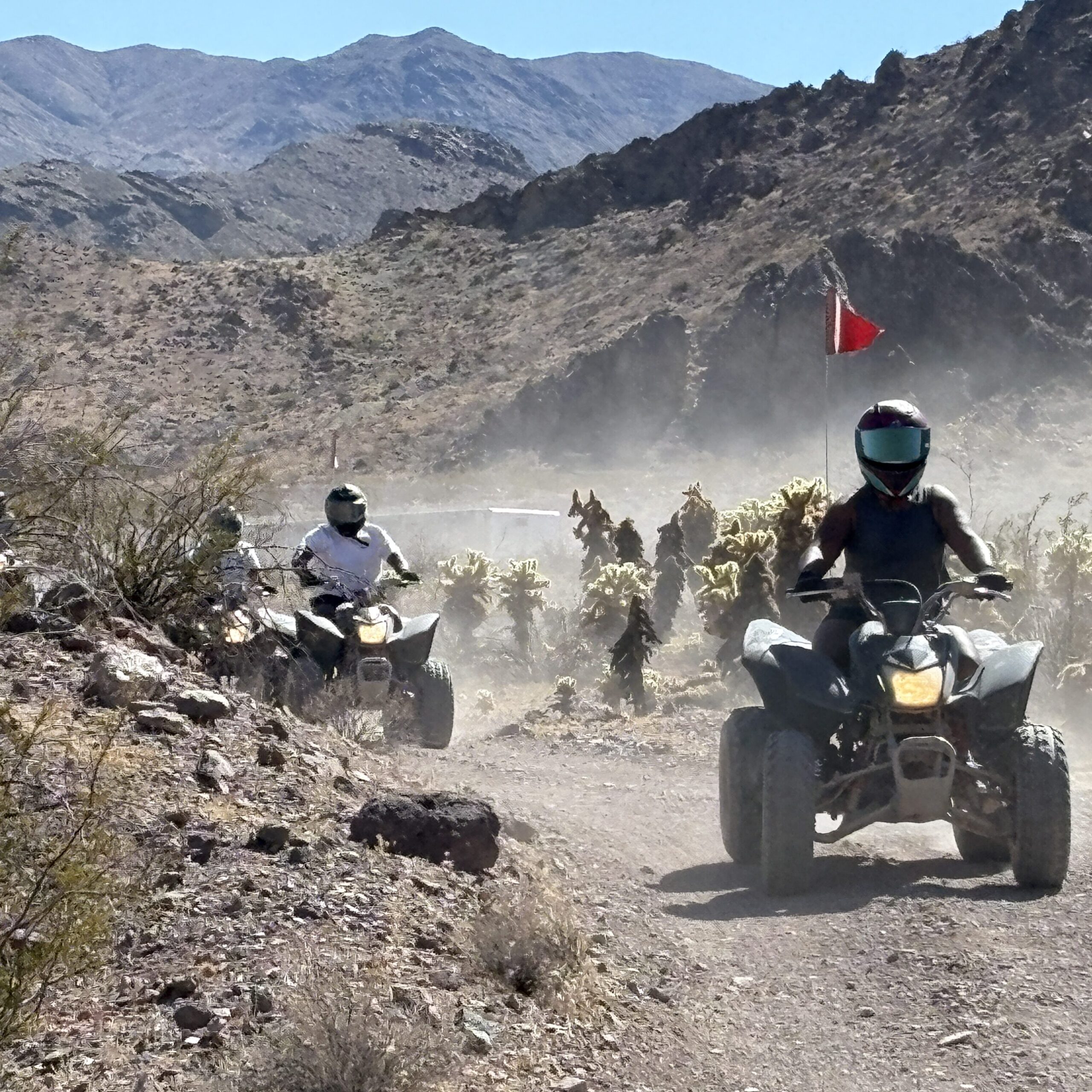 Adventurers on ATVs tour a dusty Nevada desert trail near Las Vegas, surrounded by rocky hills, cacti, and distant mountains.