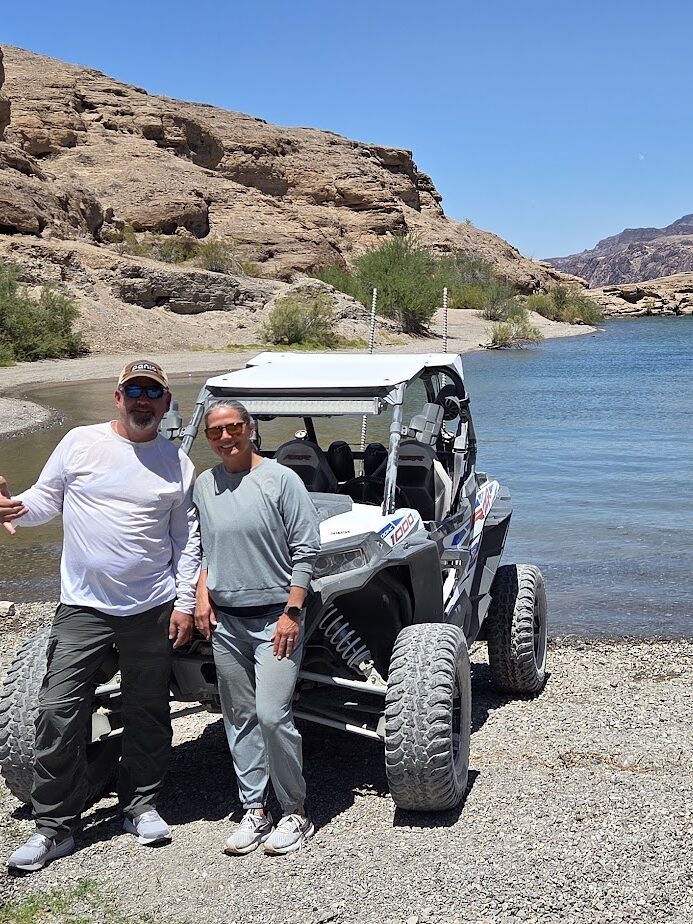 Smiling duo by an off-road RZR on the Colorado River near Las Vegas, Nevada, ready for scenic ATV tours and adventure.