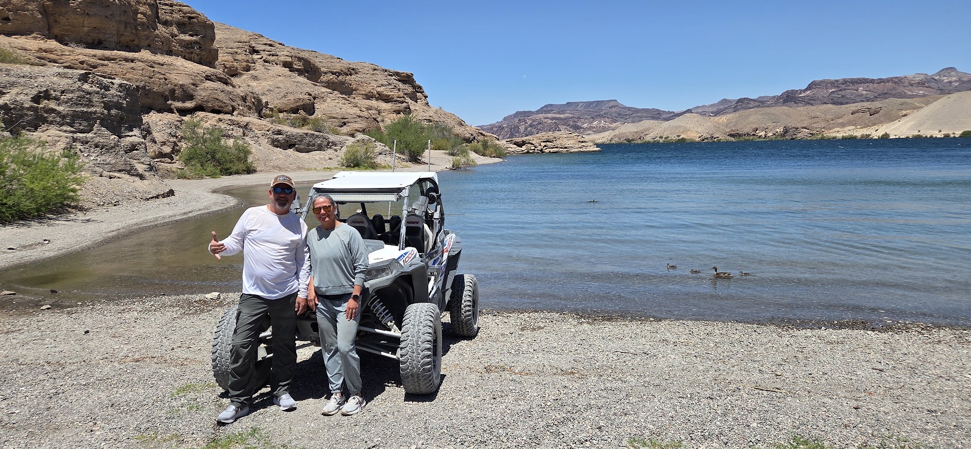 Smiling duo by an off-road RZR on the Colorado River near Las Vegas, Nevada, ready for scenic ATV tours and adventure.