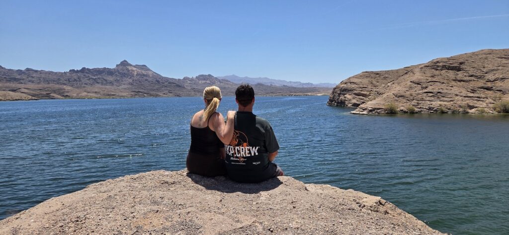 Couple on rocky ledge by Colorado River near Las Vegas, Nevada, overlooking lake and mountains—ideal for ATV tours and sightseeing.
