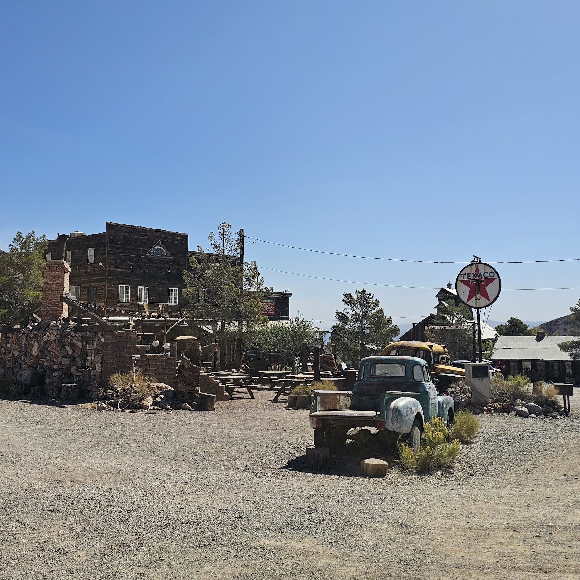 Vintage Texaco sign, blue truck, and rustic buildings in a Nevada ghost town near the Colorado River—perfect for sightseeing tours.