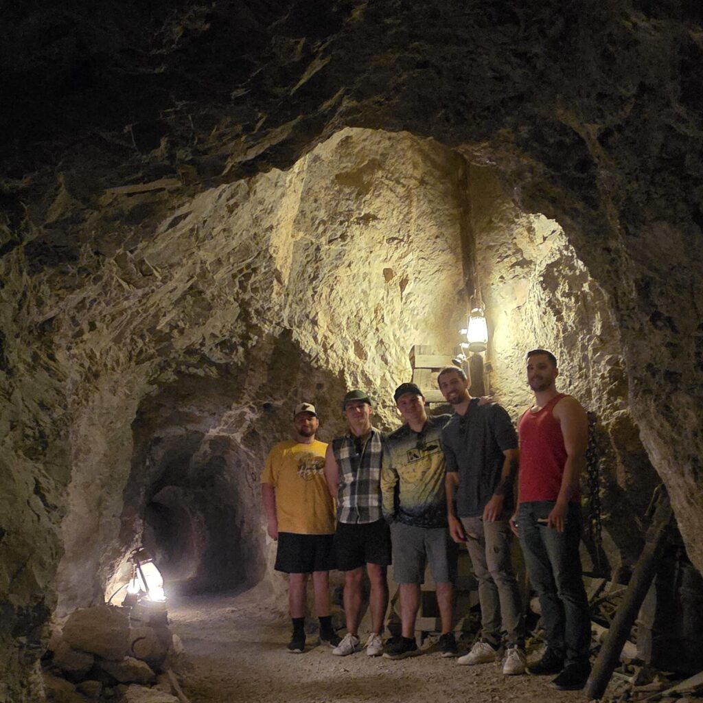 Group stands in a dim Las Vegas tunnel, lit by lanterns, on rocky ground—perfect for Ghost Town sightseeing or ATV tours.