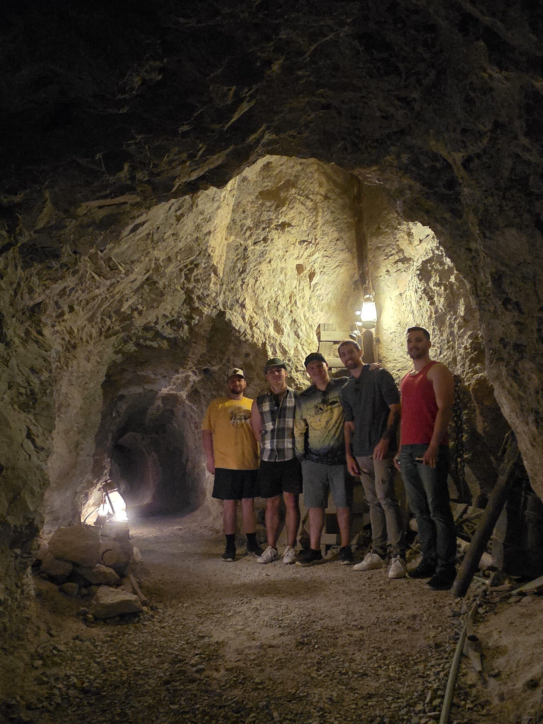 Group stands in a dim Las Vegas tunnel, lit by lanterns, on rocky ground—perfect for Ghost Town sightseeing or ATV tours.