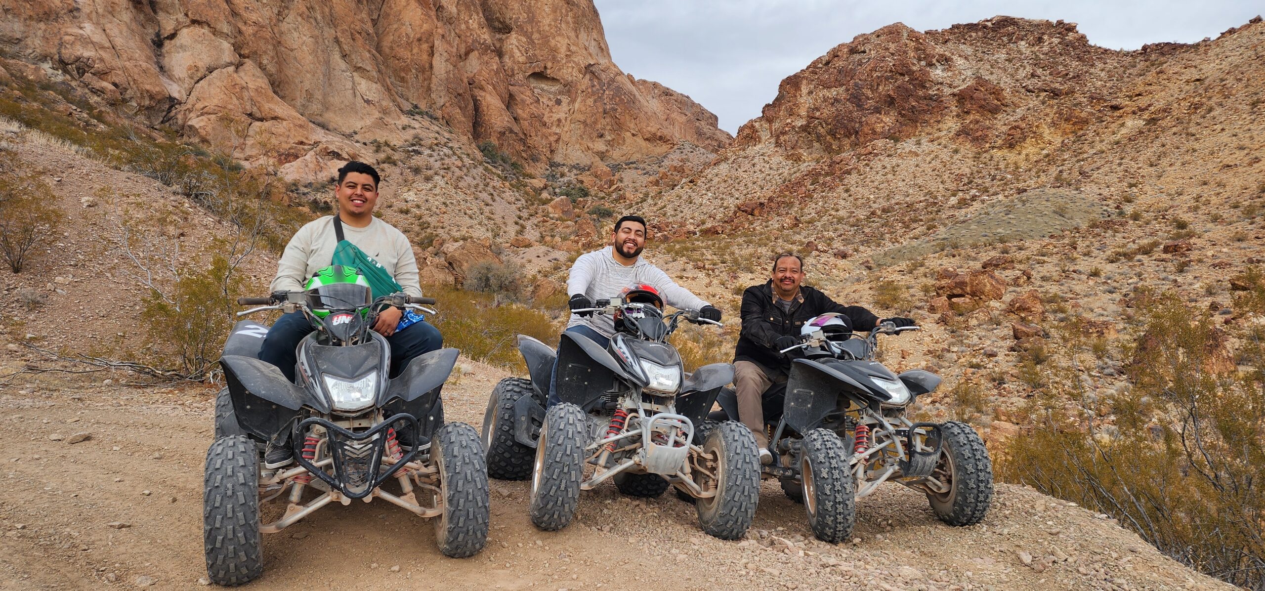 Three people enjoy an ATV tour near Las Vegas, riding through Nevada’s desert trails with rocky mountains and sparse vegetation.