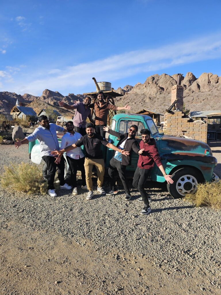 Group smiles by a turquoise vintage truck in Las Vegas, Nevada, set for ATV tours and Ghost Town sightseeing near desert mountains.