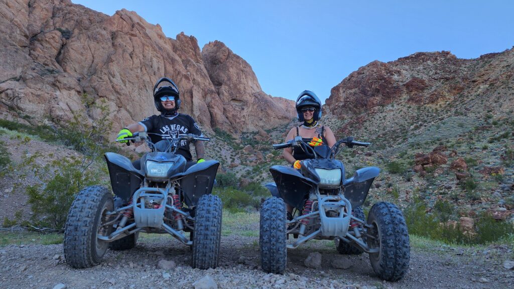 Smiling riders on ATVs, helmets and sunglasses on, explore Nevada’s desert near Las Vegas—perfect for ATV tours or RZR adventures.