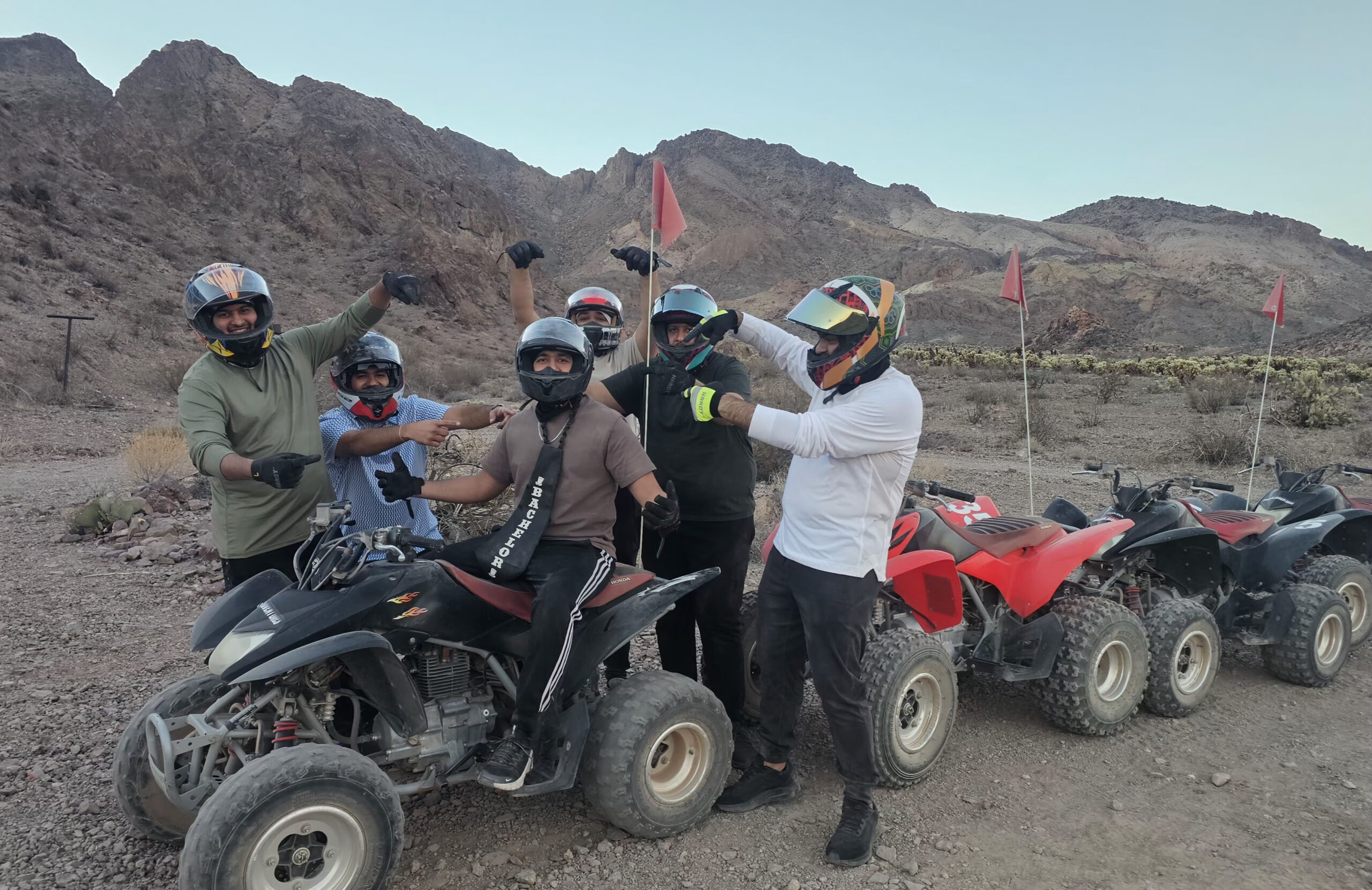 Group of six in helmets pose by four ATVs with red flags in Nevada’s rocky desert near Las Vegas, enjoying an ATV tour adventure.