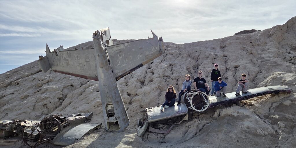 Group poses on old plane wreck at Nelson Ghost Town near Las Vegas, Nevada—perfect for ghost town tours and sightseeing adventures.