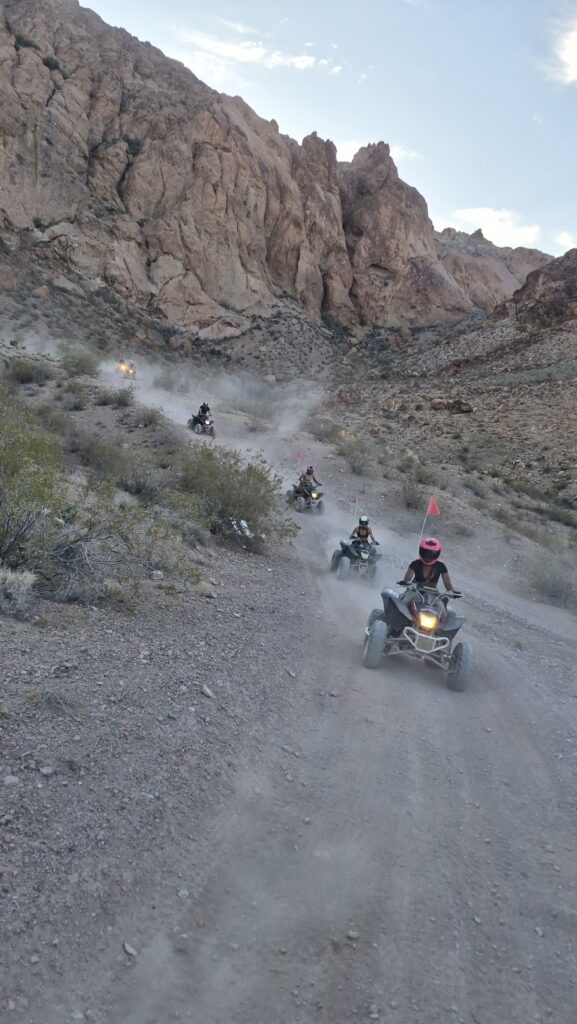 Adventurers enjoy an ATV tour on a dusty desert trail near rocky cliffs and shrubs in Las Vegas, Nevada.