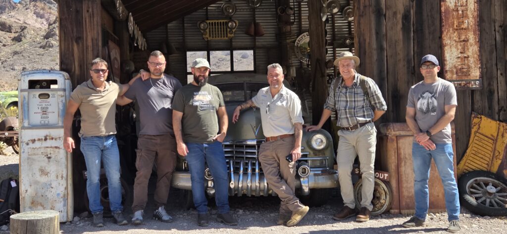 Six men pose by a vintage car in a rustic Nevada garage near Las Vegas, perfect for Ghost Town sightseeing and ATV tours.