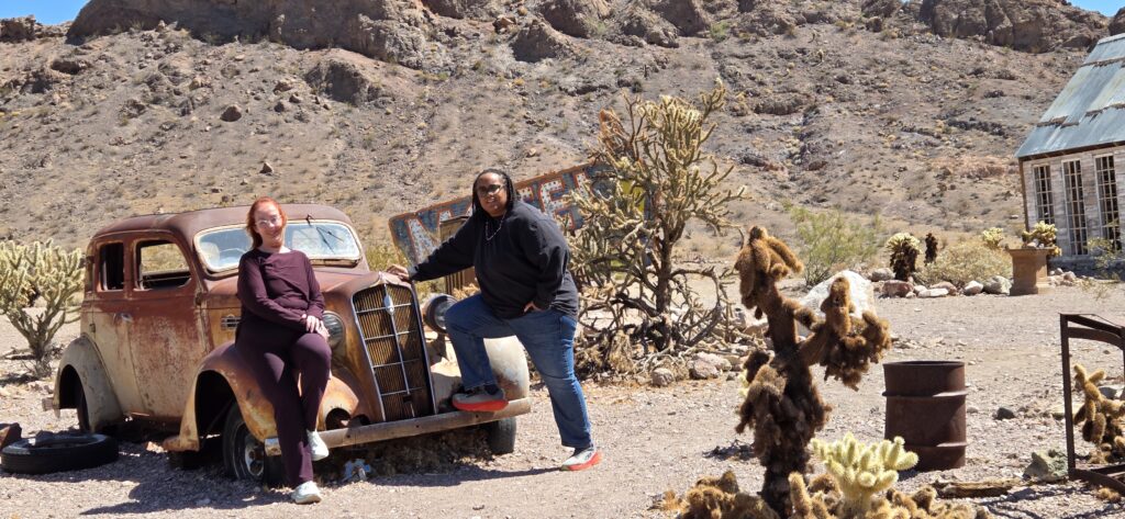 Two people pose by a rusty car in a Nevada desert near Las Vegas, perfect for Ghost Town sightseeing and off-road adventures.