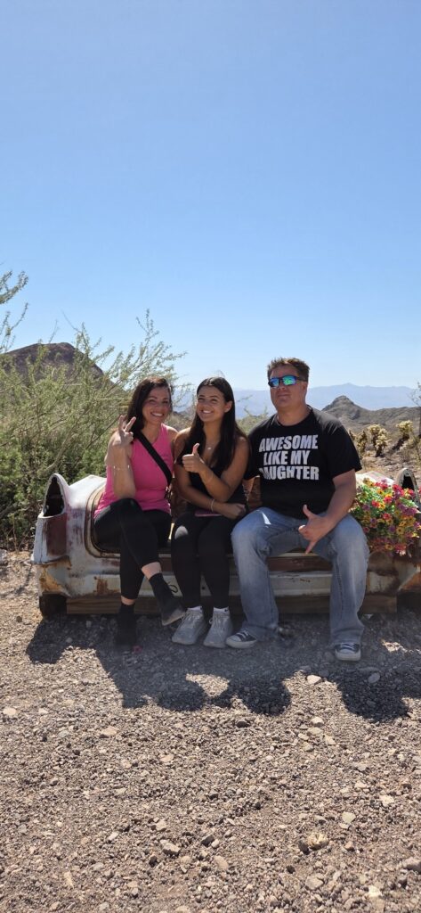 Friends pose on a rusty car in the Nevada desert near Las Vegas, flashing peace signs during Ghost Town sightseeing.