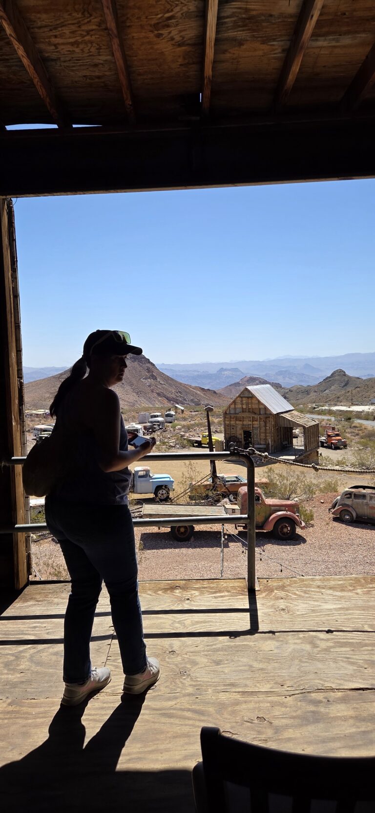 A visitor in a wooden structure overlooks a Nevada ghost town near Las Vegas, with old cars and mountains—ideal for Ghost Town sightseeing.