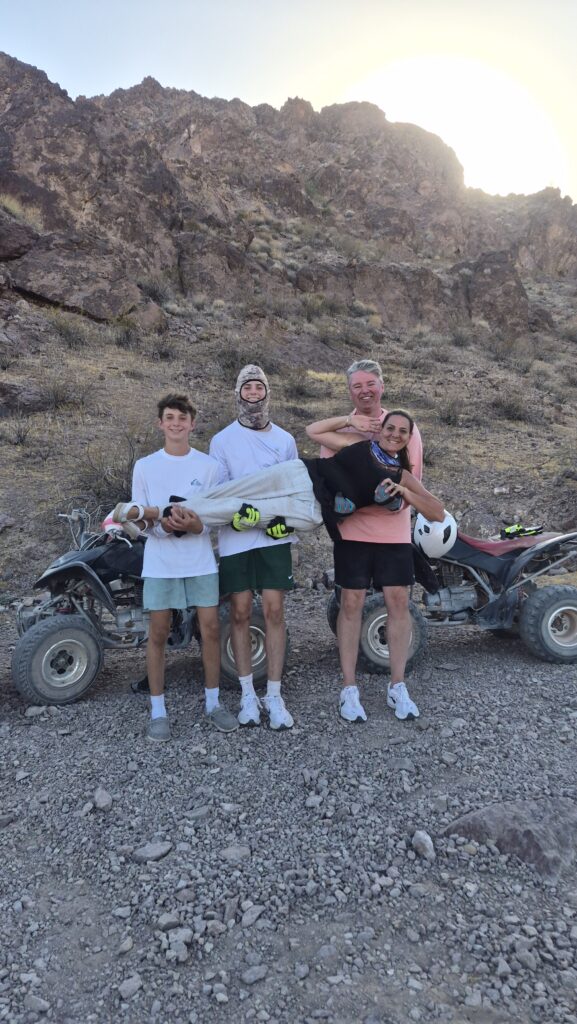 Group smiles with helmets in front of two ATVs at sunset on Nevada rocky terrain near Las Vegas, ready for an ATV tour adventure.