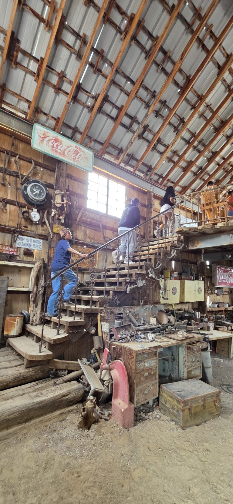 Visitors explore a rustic Nevada workshop filled with vintage items and tools, sunlight streaming in; perfect for Ghost Town sightseeing.