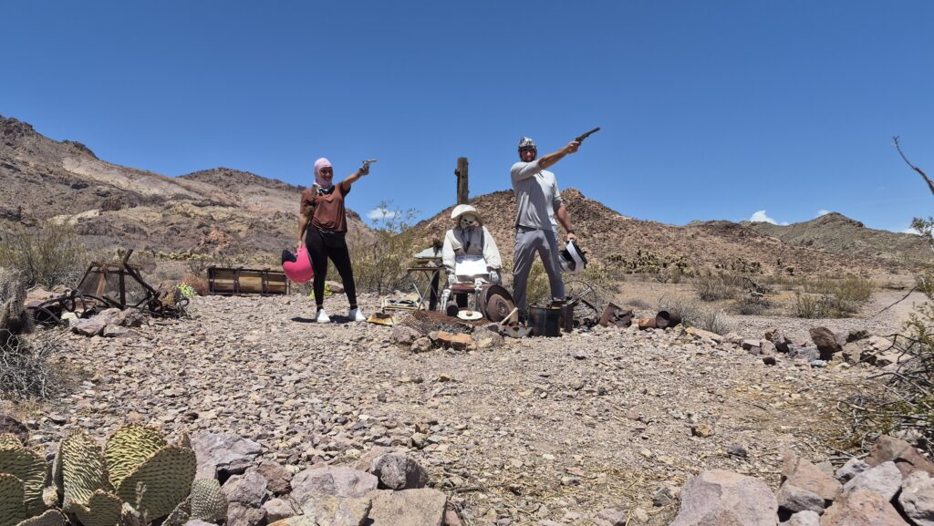 Three in western outfits pose by cacti and rocks near Las Vegas, Nevada, with props; perfect for Ghost Town sightseeing photos.