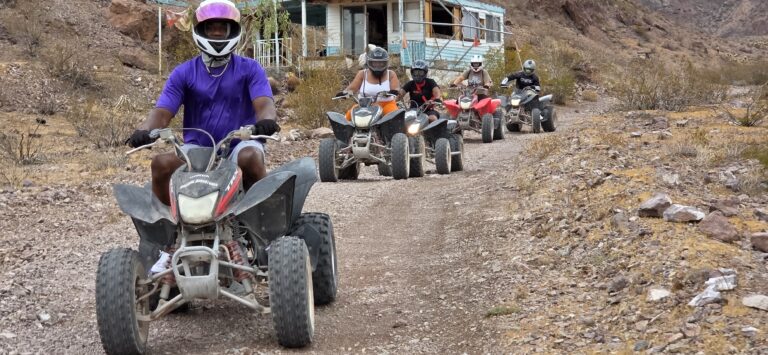 Group enjoys an ATV tour near Las Vegas, riding past a weathered blue house on a rocky Nevada desert trail.