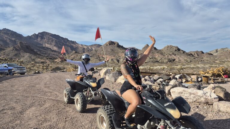 Riders on an ATV tour near Las Vegas, Nevada, celebrate on a rocky desert trail with mountains and a bright blue sky behind.
