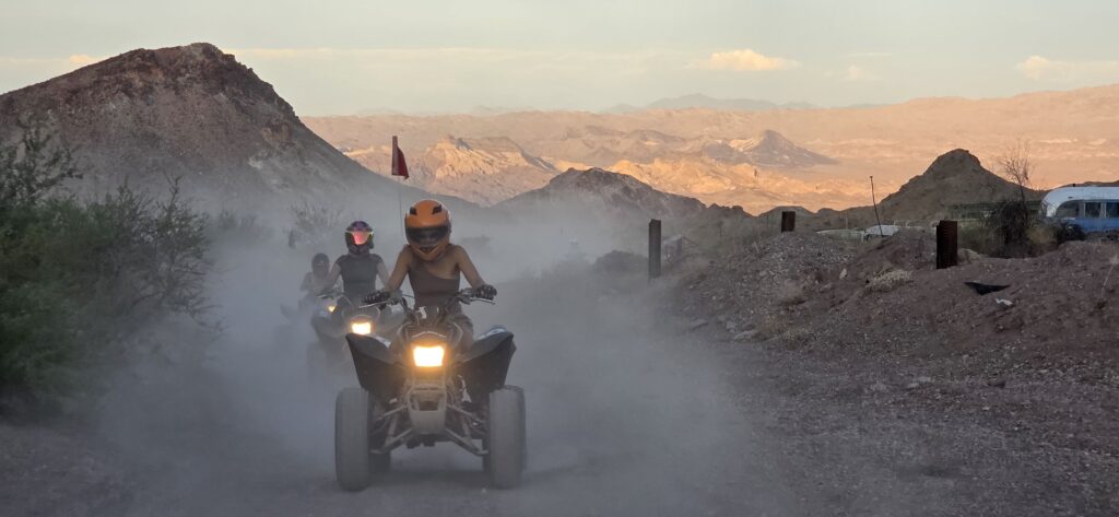 ATV riders explore a dusty Nelson, Nevada ghost town trail near Las Vegas, with mountains and desert scenery in the background.