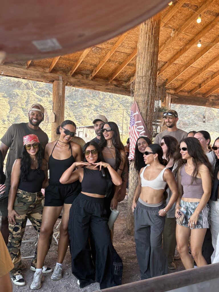 Friends smiling under a wooden roof in Las Vegas, Nevada, with mountains and an American flag—perfect for ATV tours or Ghost Town sightseeing.