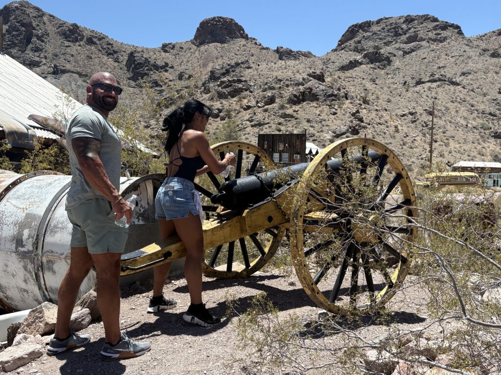 Couple by vintage yellow cannon in Nevada desert near Las Vegas, perfect for Ghost Town sightseeing and ATV tours.