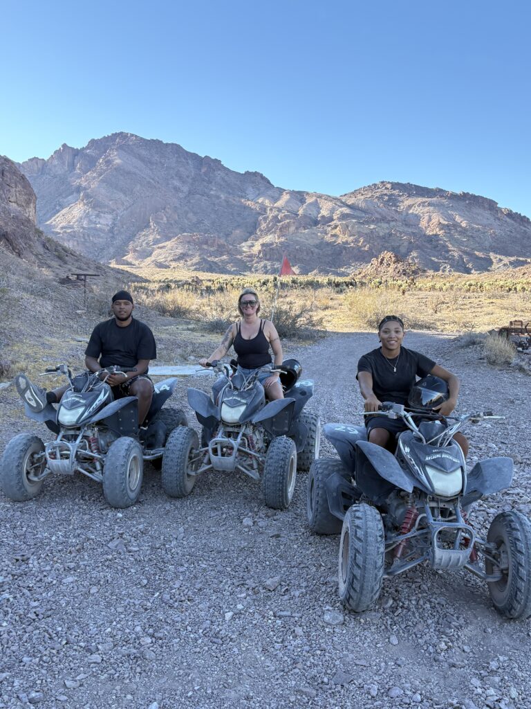 Three riders on ATVs in Nevada desert near Las Vegas, ready for an off-road ATV tour with mountains and blue sky behind them.