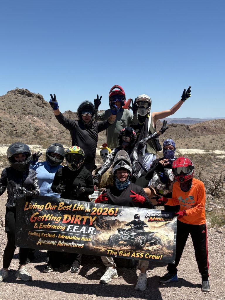 Adventurers in helmets pose by Nevada’s rocky desert near Las Vegas, holding a banner after an epic RZR ATV tour and Colorado River ride.