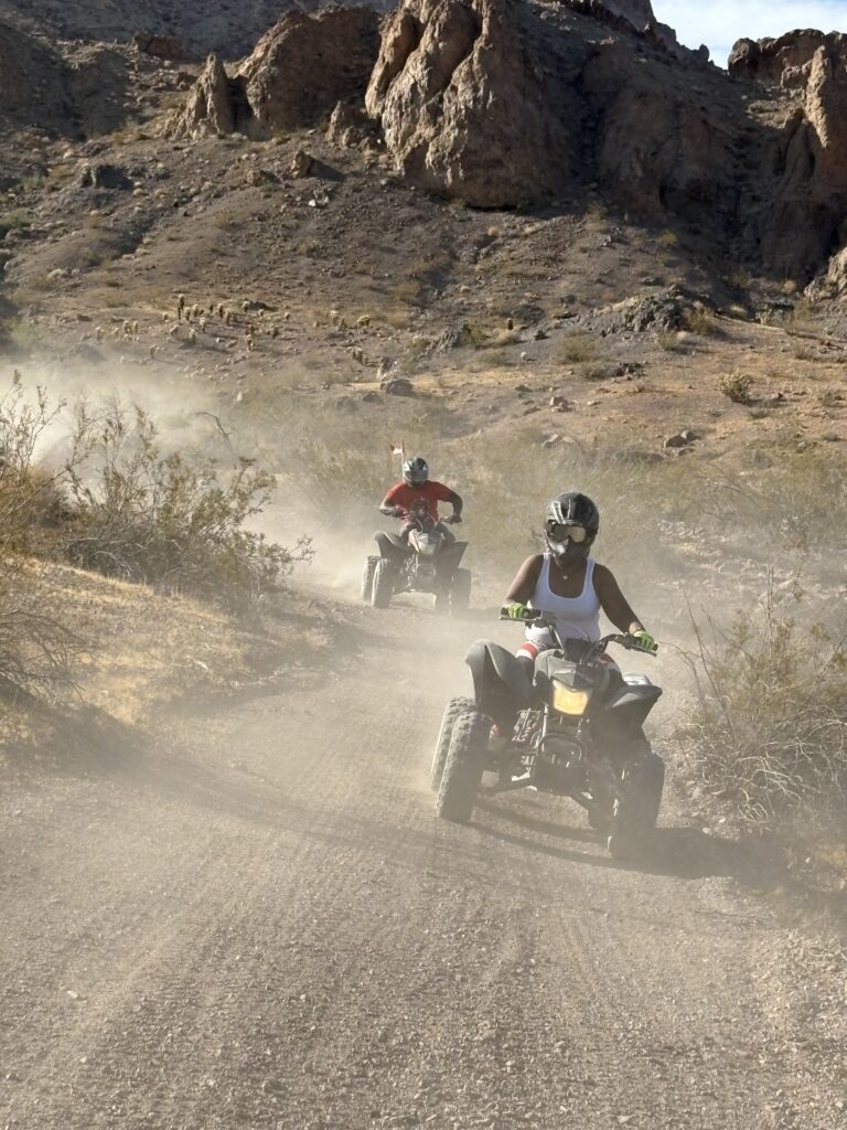 Adventure seekers ride ATVs on a dusty Nevada trail near Las Vegas with rocky hills, perfect for ATV tours and off-road excitement.